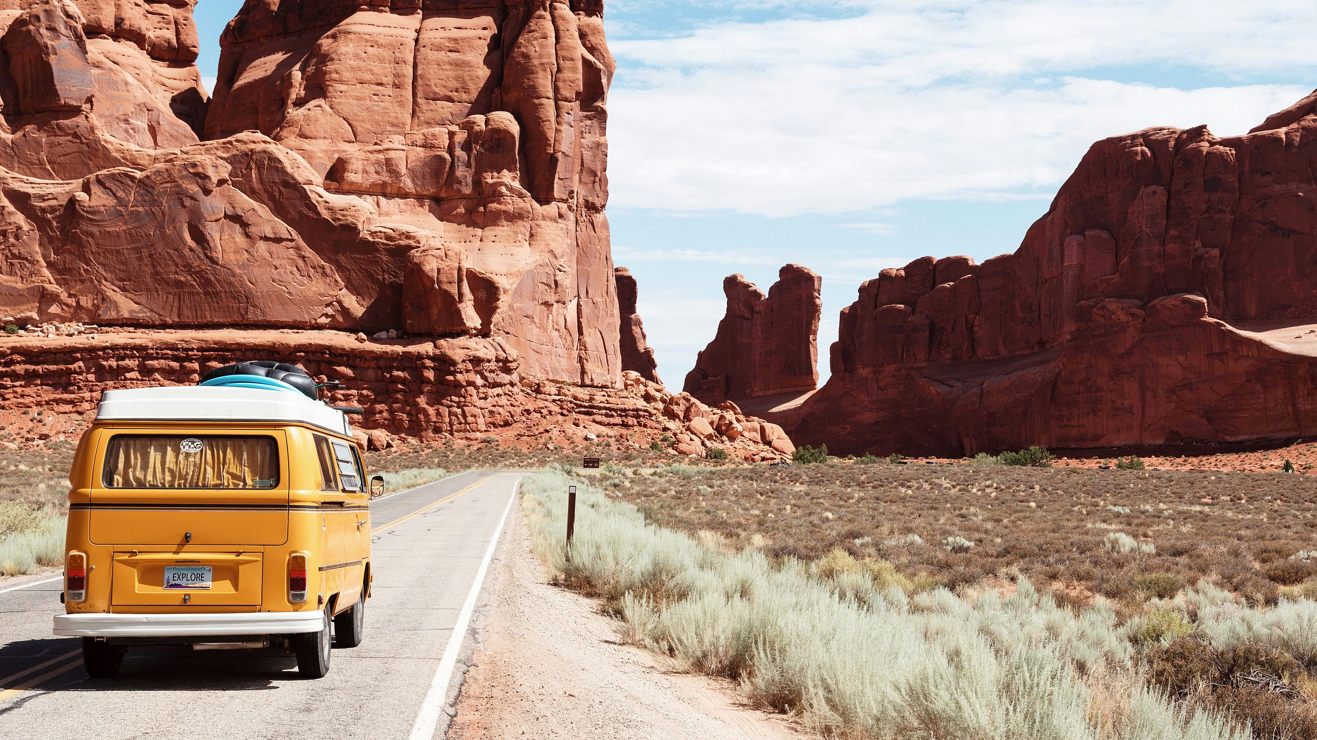 Charming vintage van traveling through stunning red rock canyons under a vibrant sky, embodying adventure and exploration.