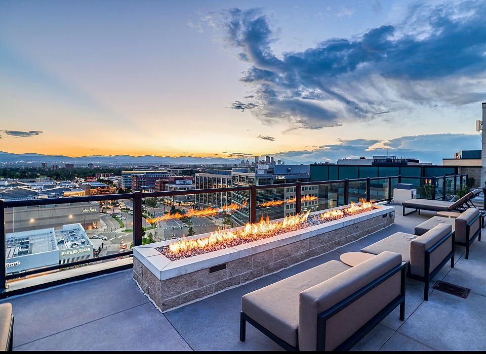 Luxurious rooftop terrace with modern fire pit, offering breathtaking cityscape and mountain views at sunset.