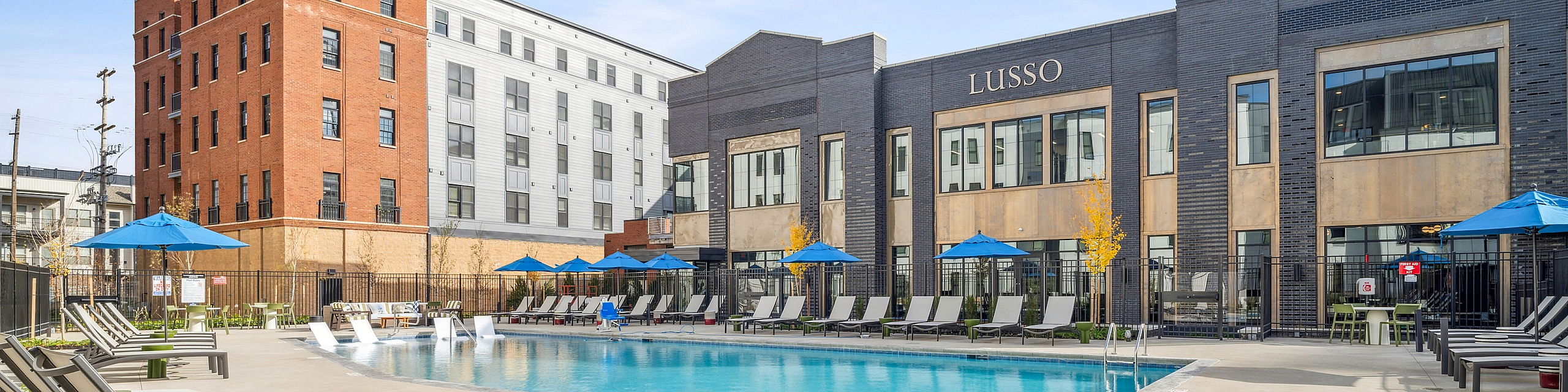 Luxurious apartment complex with modern poolside lounge, sun umbrellas, and chic seating, perfect for relaxation.