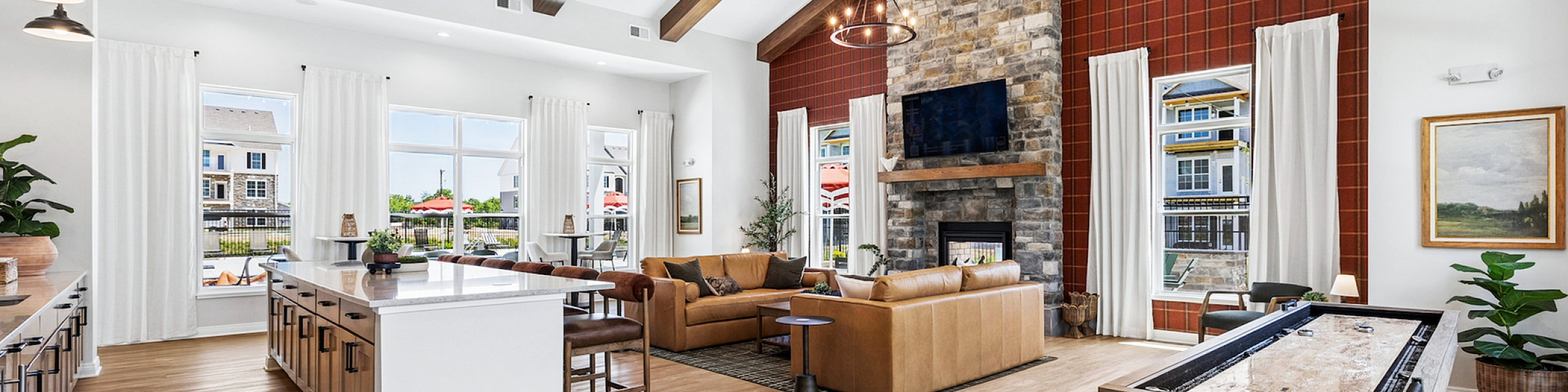 Luxurious open-concept living room with vaulted ceilings, elegant wood beams, and a stunning stone fireplace. Spacious interior features a modern kitchen island, cozy seating area, and large windows with abundant natural light.