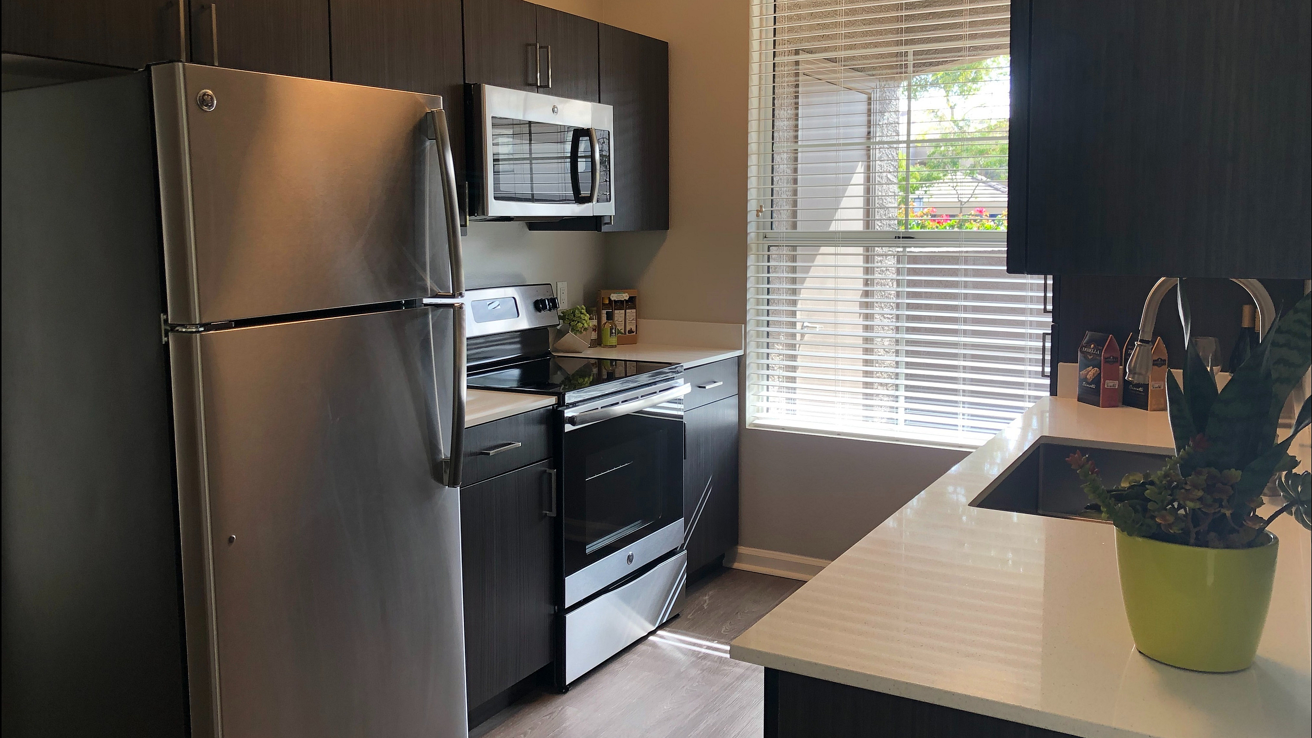 Modern kitchen with stainless steel appliances, sleek cabinets, and large window offering natural light.