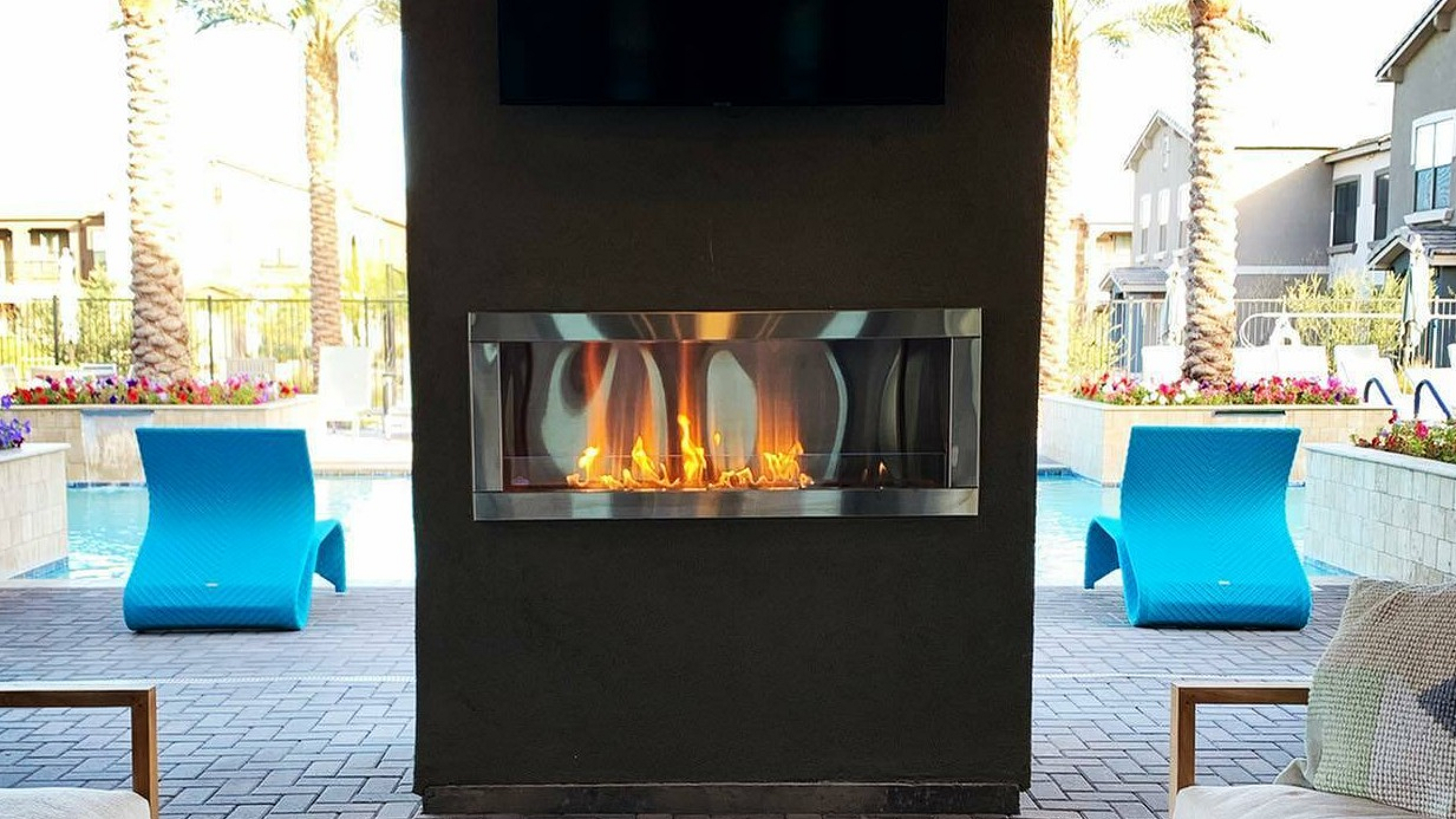 Luxurious outdoor lounge with cozy seating, modern fireplace, and inviting poolside view under palm trees.