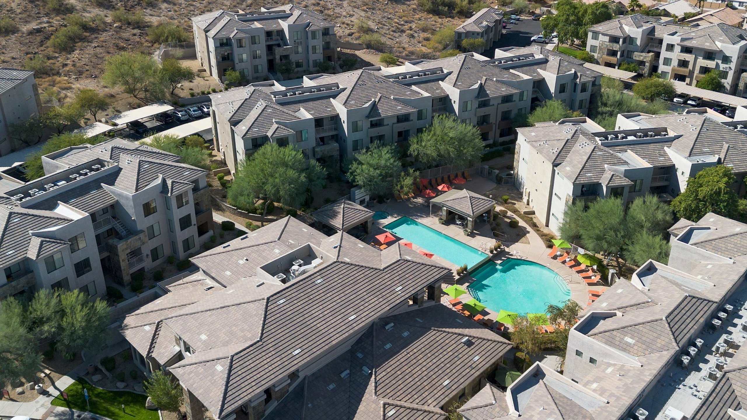 Luxurious apartment complex with stunning mountain views, featuring a sparkling pool surrounded by modern architecture and lush greenery.