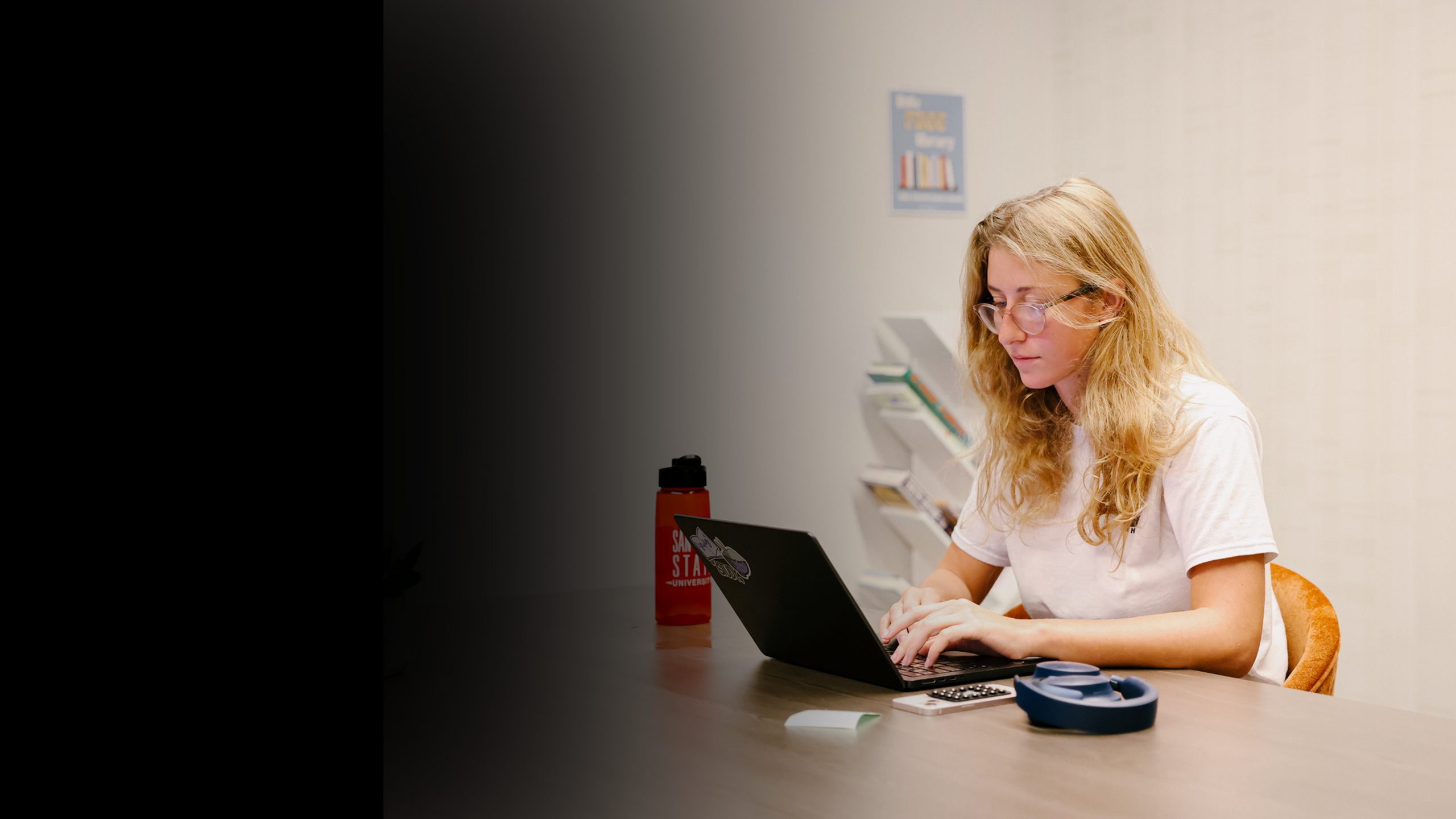 Student working on a laptop at a table in a quiet apartment community study room, featuring comfortable seating and a focused environment ideal for student living.
