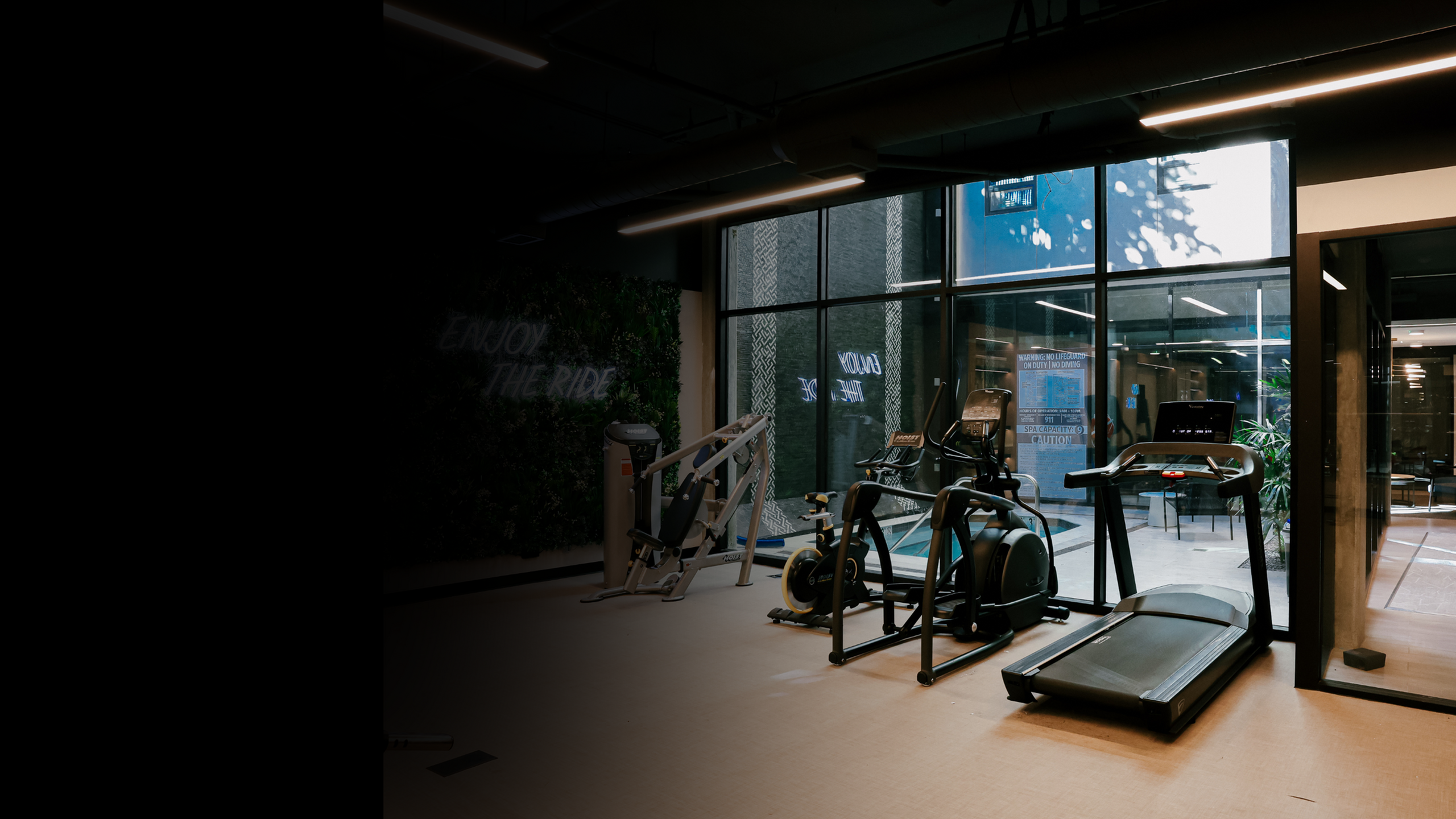 Modern apartment fitness center with treadmills, stationary bikes, strength equipment, and floor-to-ceiling windows bringing in natural light, offering residents a convenient on-site gym for everyday workouts.