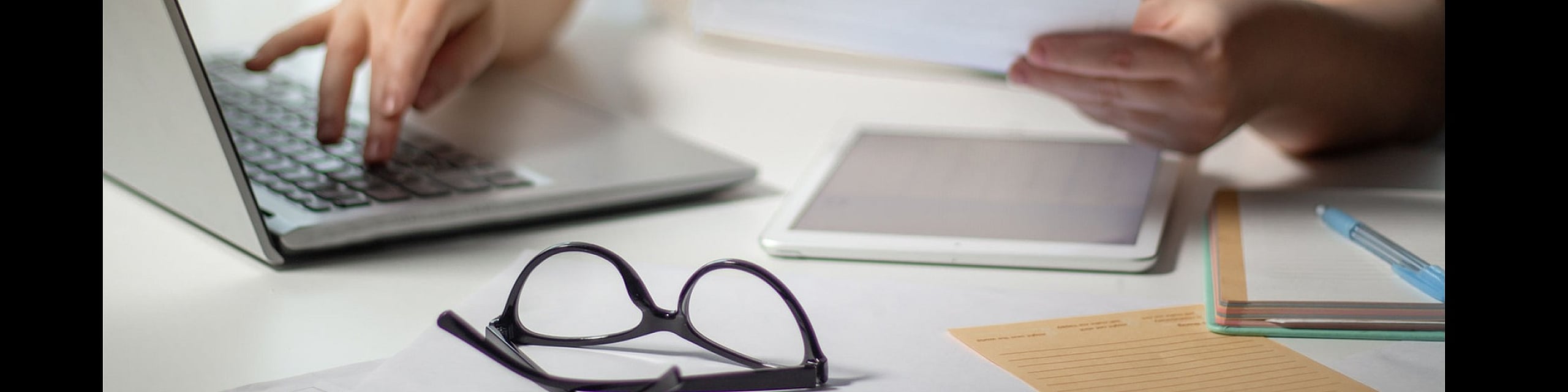 Cozy workspace setup with a laptop, documents, and glasses on a white desk, perfect for productivity.