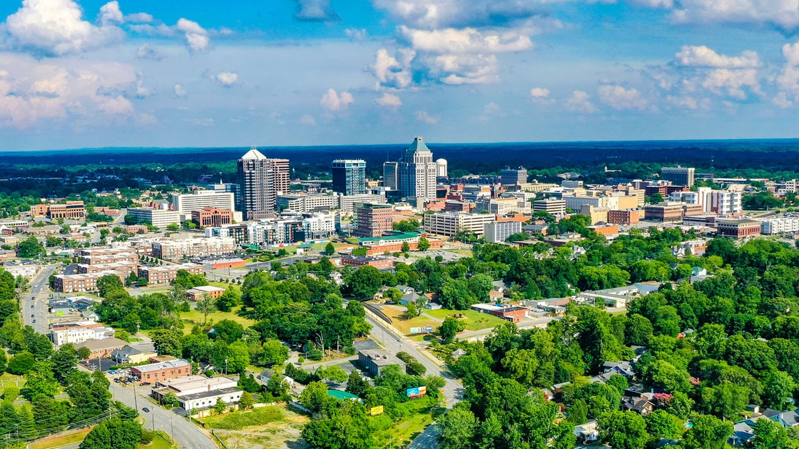 Vibrant aerial view of a lush, green cityscape with modern high-rise buildings under a bright blue sky, showcasing urban living at its best.