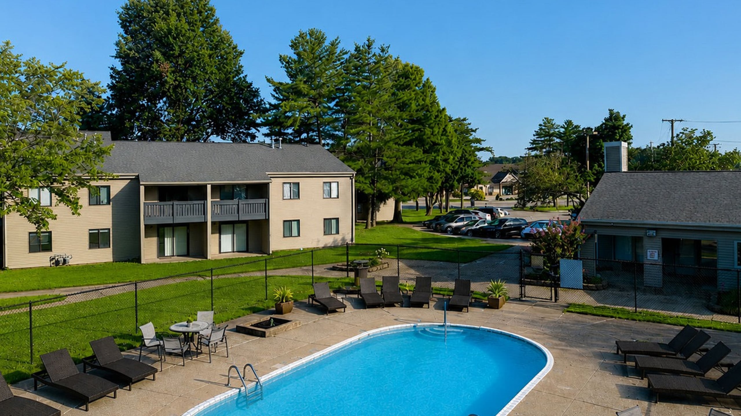 Inviting community pool area with lounge chairs and tables, surrounded by lush greenery and modern apartments.