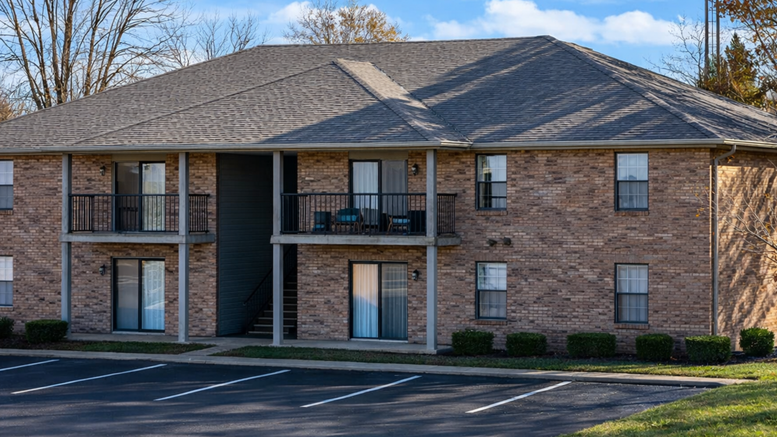 Charming two-story brick apartment building with inviting balconies, set in a serene landscaped environment.