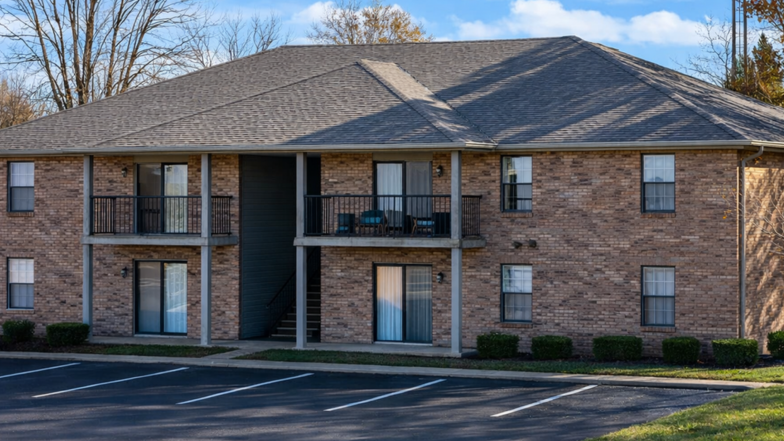 Charming two-story brick apartment building with private balconies and ample parking, set against a clear blue sky.