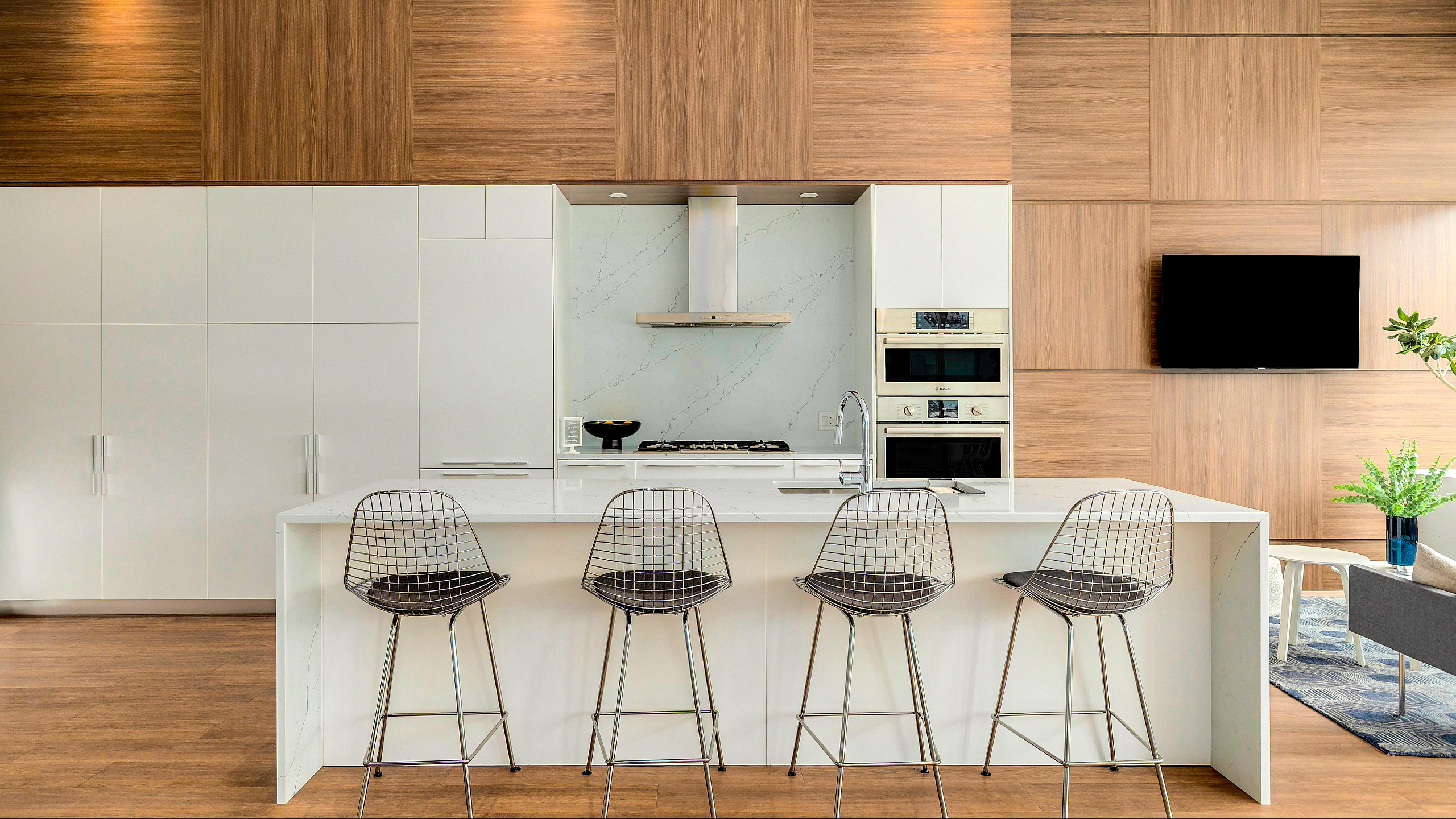 Sleek modern kitchen with a stylish island and four contemporary bar stools, complemented by elegant wood paneling and built-in appliances.
