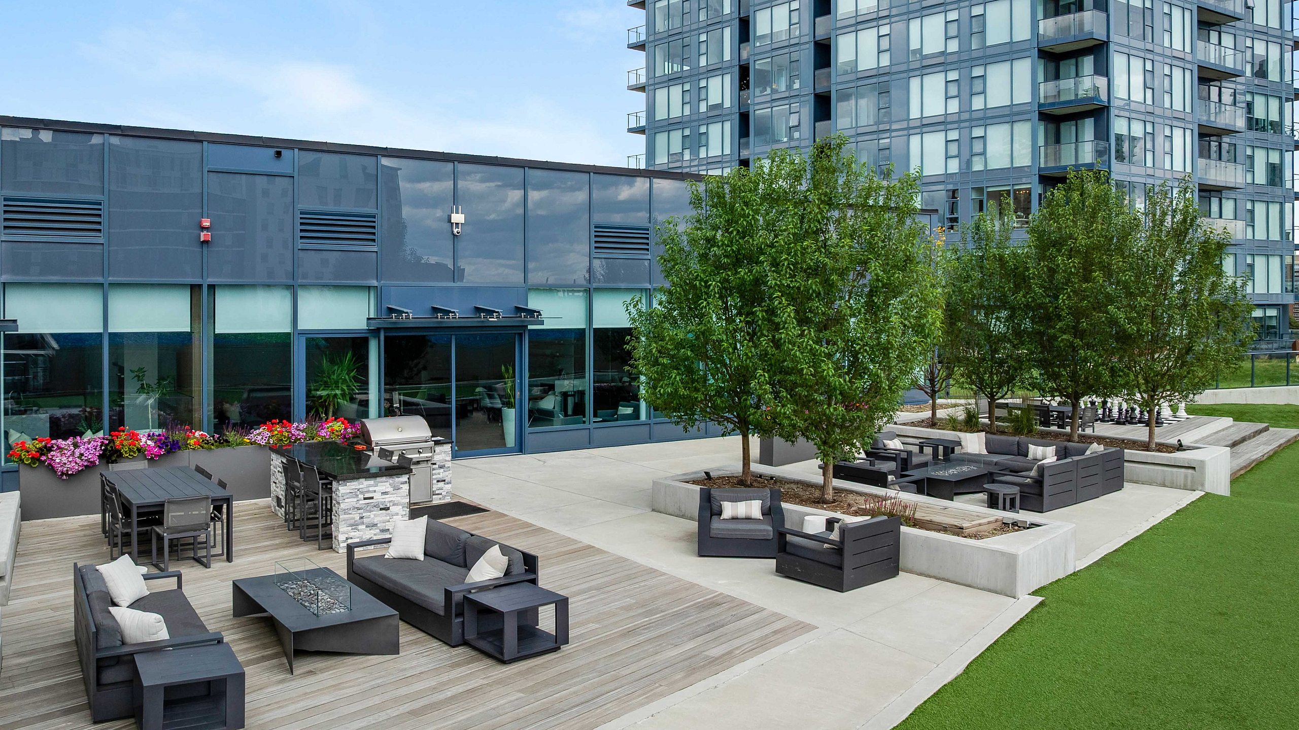 Luxurious high-rise apartment with a spacious outdoor lounge area, featuring modern seating, green spaces, and vibrant flower arrangements.