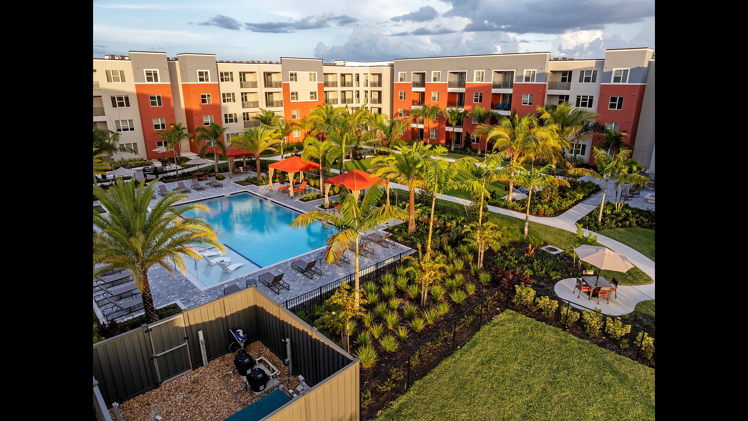 A vibrant apartment complex with a large pool, lush landscaping, and modern architecture.