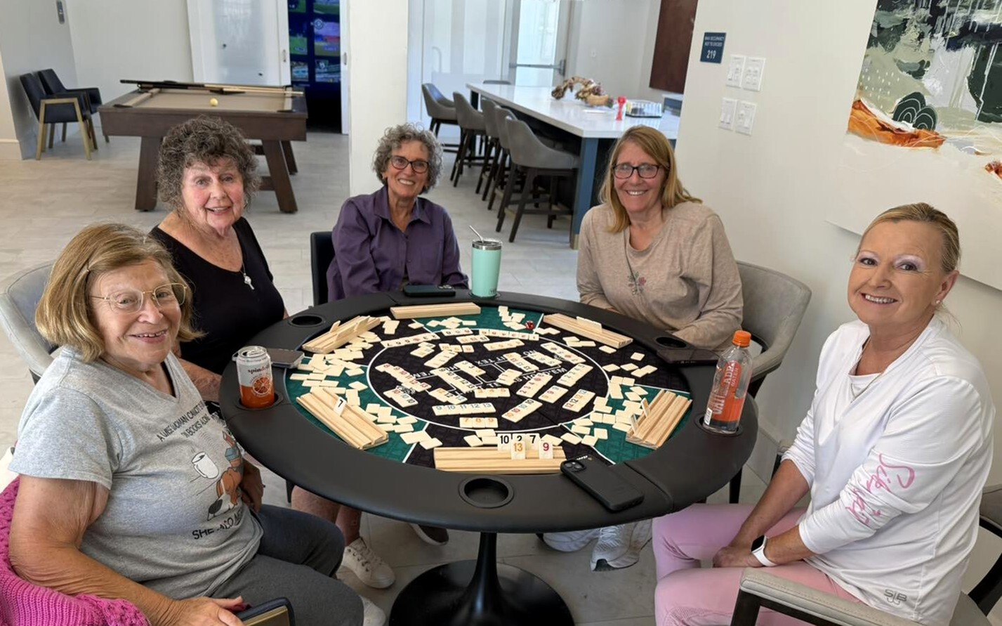 Group of residents playing a tile game around a table in the clubhouse
