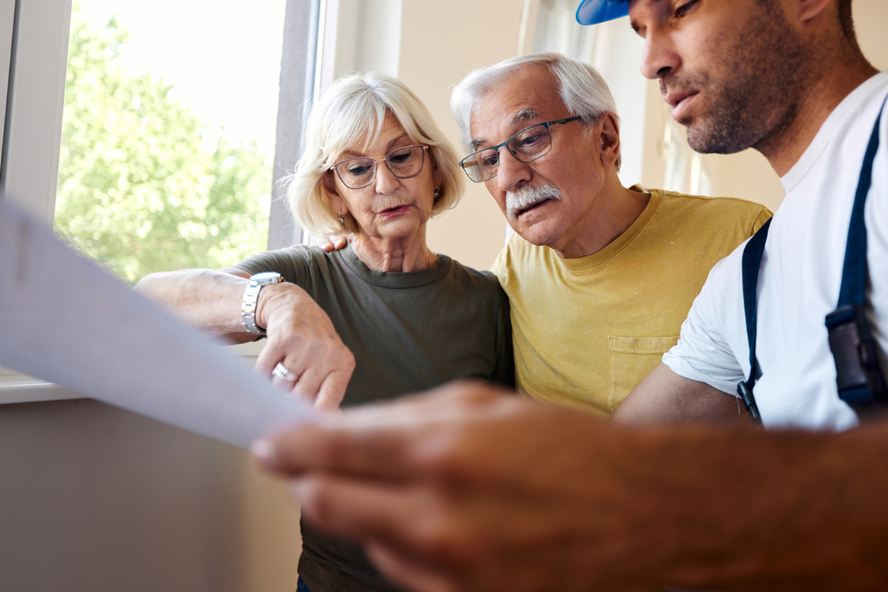 Mature couple examining blueprints with manual worker during home renovation process