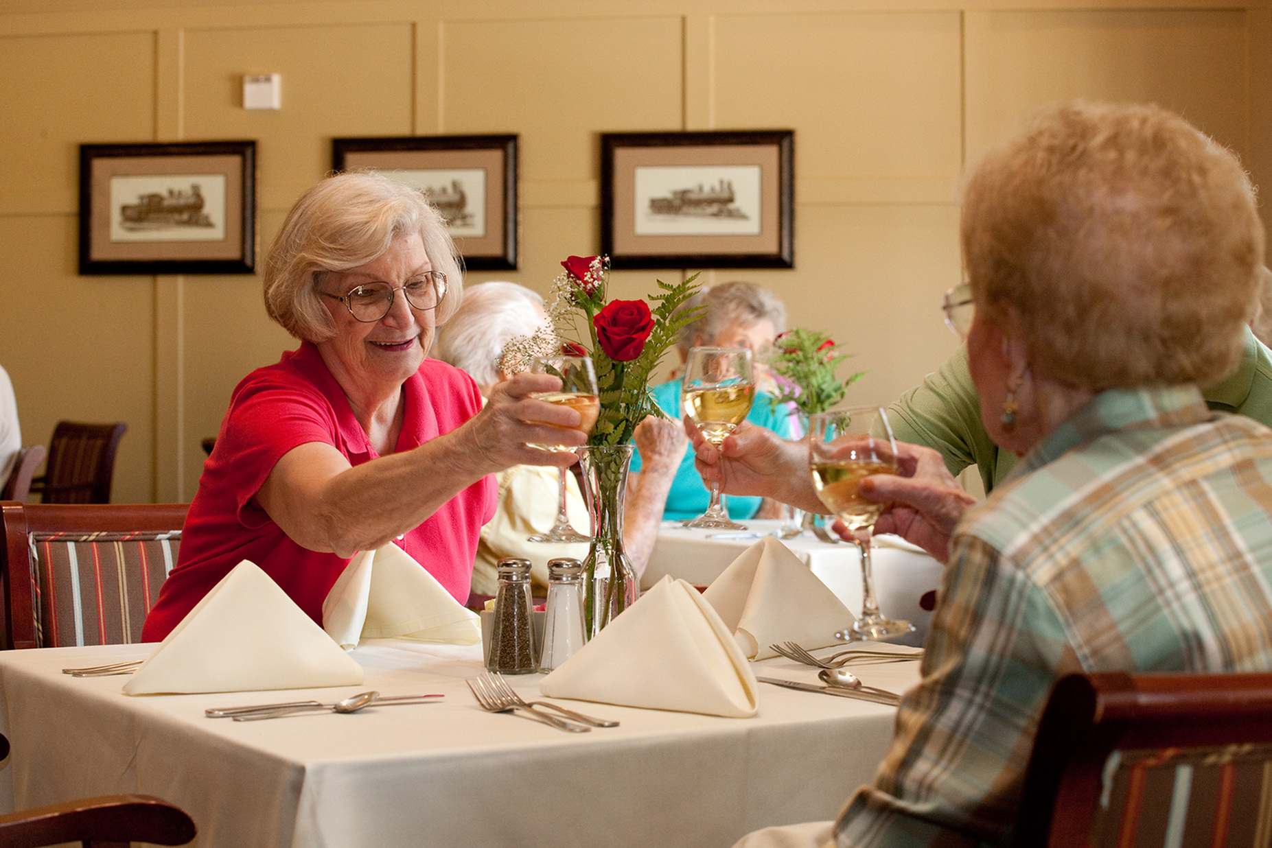 Residents sitting at a table in The Lodge at BridgeMill's restaurant, smiling and toasting with each other