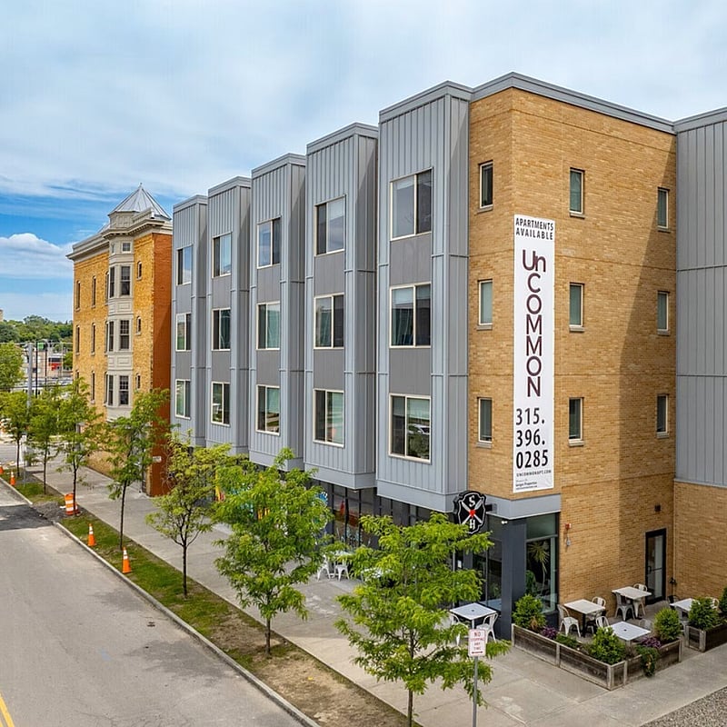 Contemporary urban apartment building with stylish facade, featuring large windows and outdoor seating area, ideal for modern living.
