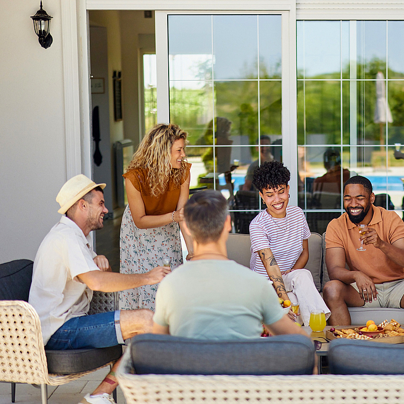 Lively outdoor gathering at the Kensington pool patio, featuring a group of friends enjoying drinks and snacks in a cozy seating area.