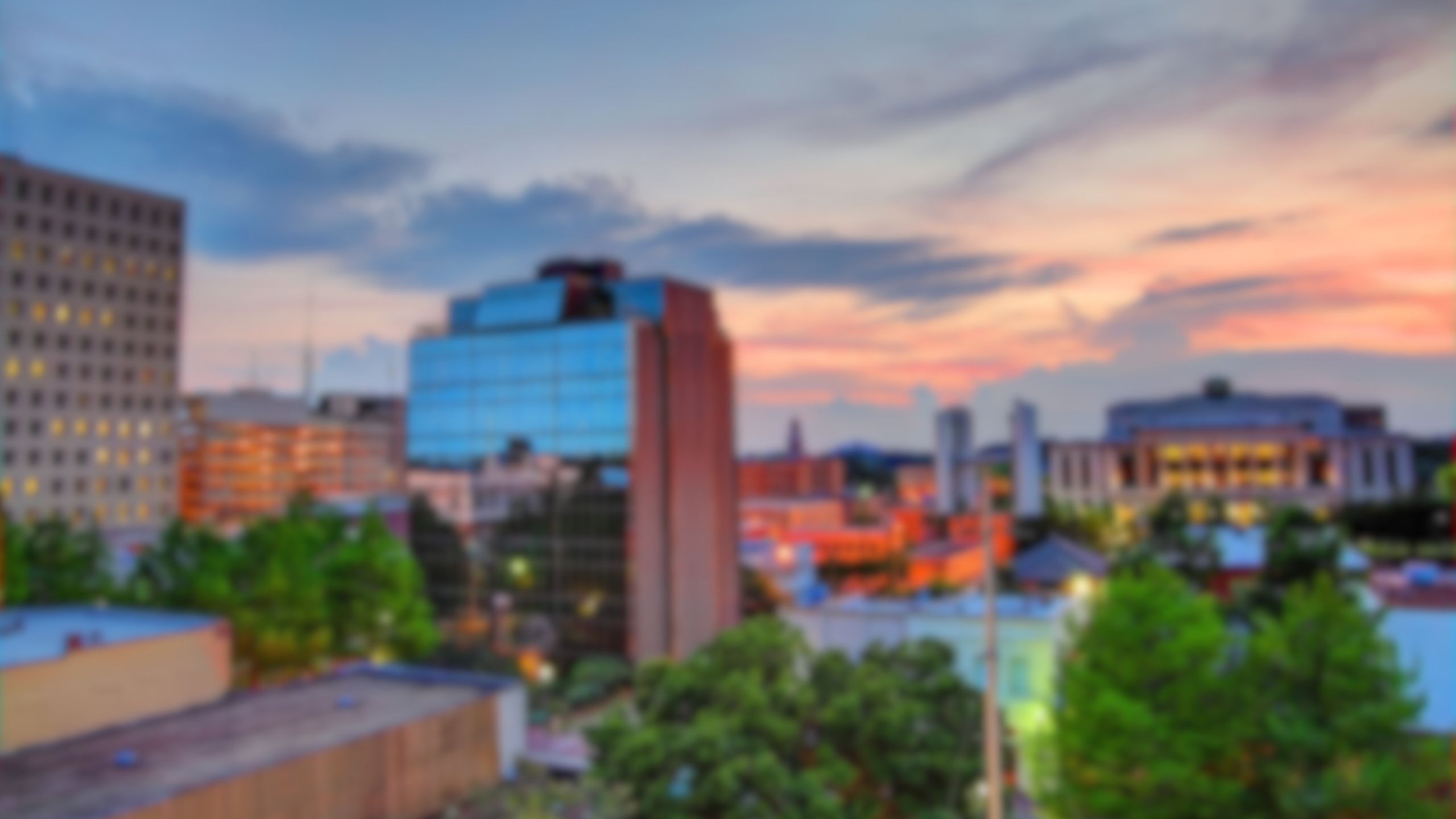 Vibrant urban skyline at sunset with modern glass buildings and lush greenery.