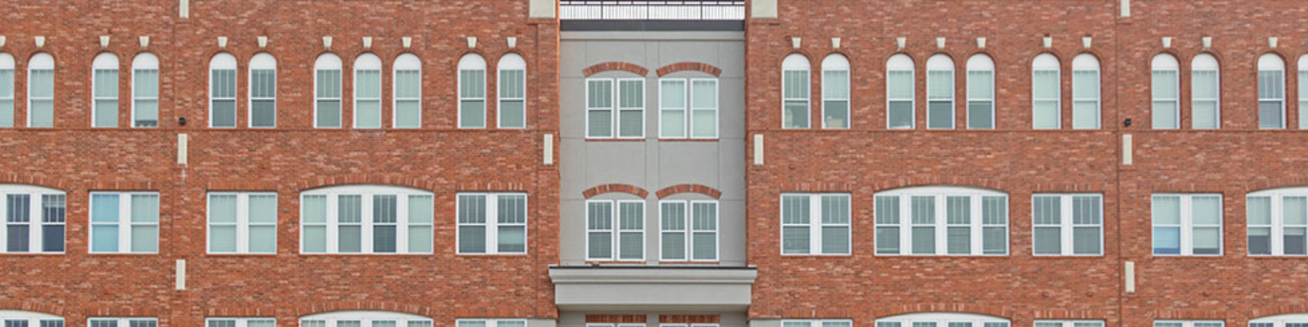 Exterior view of Chesterfield Lofts showcasing red brick architecture with arched windows and modern gray accents, highlighting the building’s urban design and upscale apartment living in Chesterfield Village