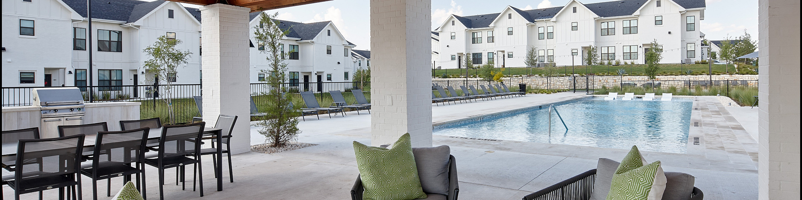 Chic outdoor lounge featuring comfortable seating, modern ceiling fans, and poolside view with stylish townhouses.
