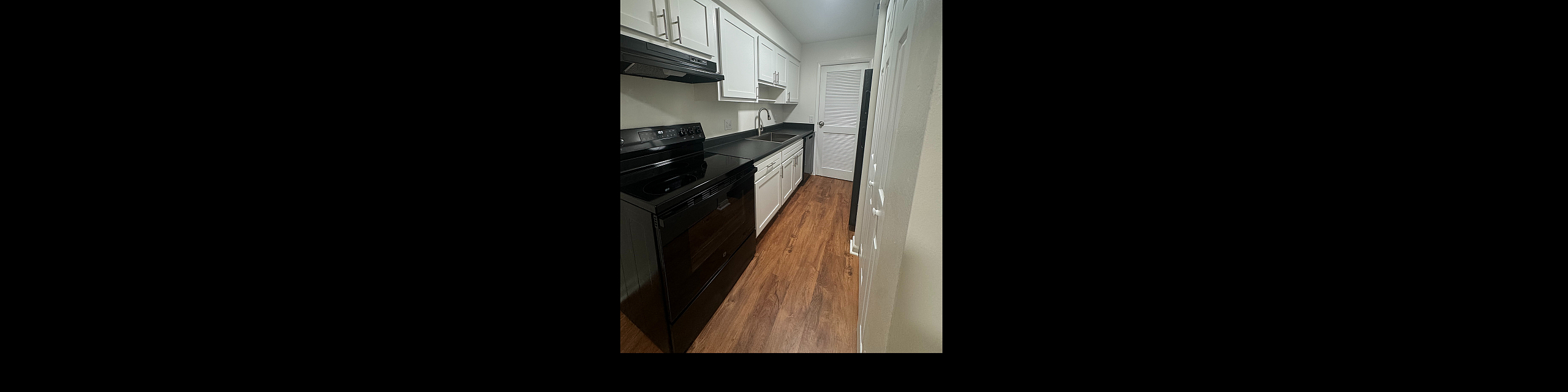 Sleek galley kitchen with modern appliances, elegant white cabinetry, and rich wood flooring.