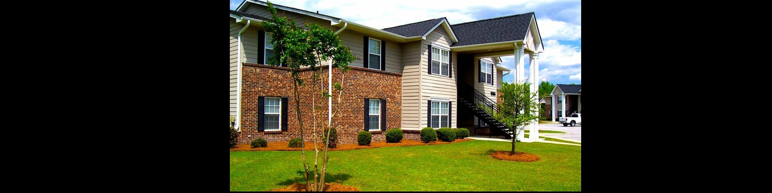Charming two-story residential building with classic brick and siding exterior, featuring lush green landscaping and inviting curb appeal.