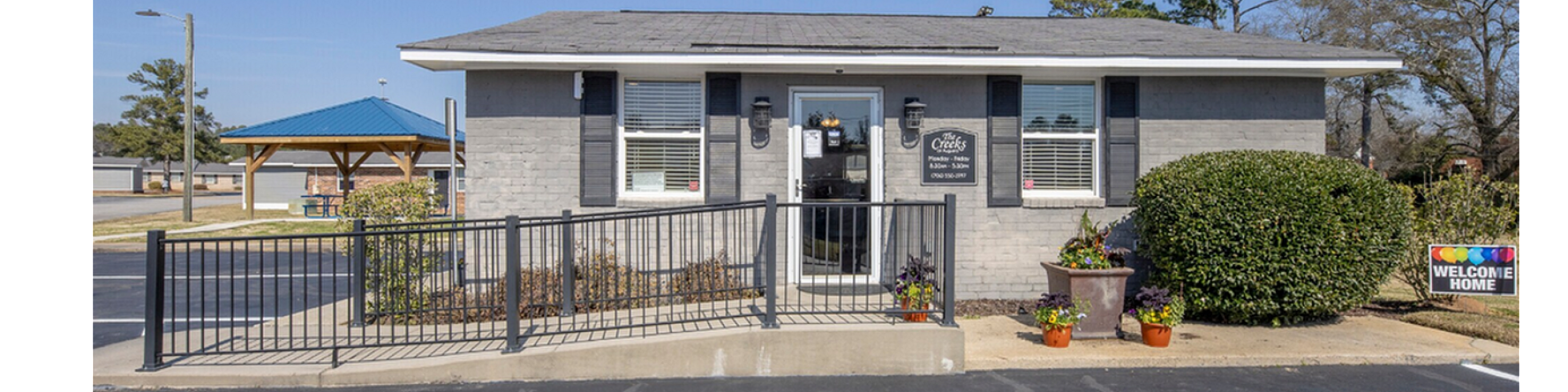 Charming community office with welcoming entrance, vibrant planters, and accessible ramp set against a clear sky for inviting curb appeal.