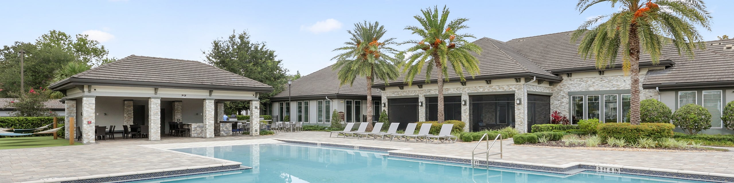 Luxurious apartment complex featuring a sparkling pool, surrounded by lush palm trees and elegant lounge chairs, perfect for relaxation and leisure.