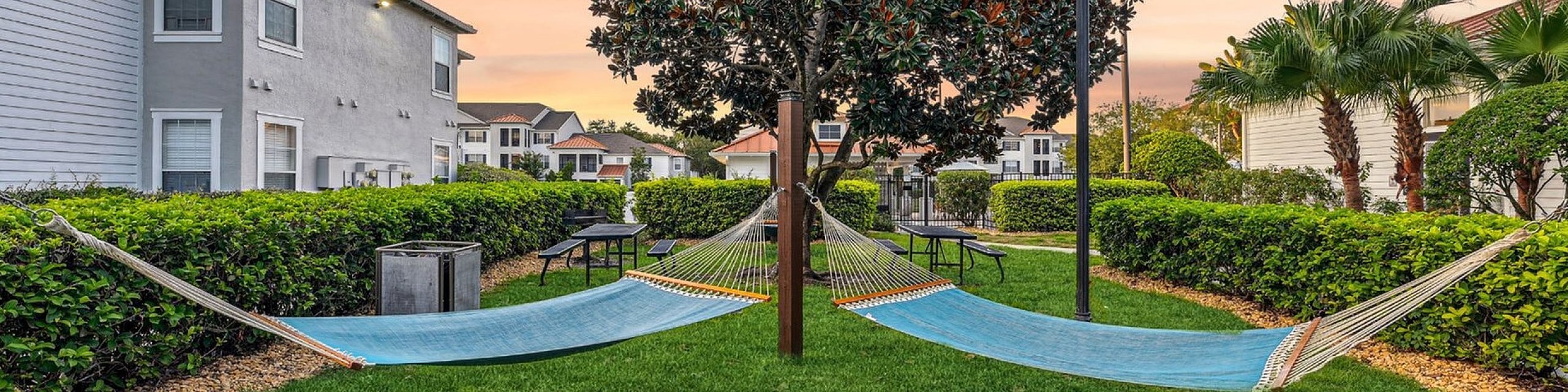 Tranquil garden setting featuring twin hammocks beside a manicured lawn and lush hedges, perfect for relaxation at sunset.