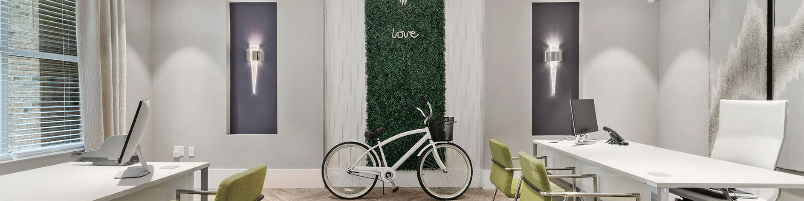 Elegant modern office space with chic decor, featuring green chairs, sleek desks, a bicycle, and decorative wall art under a stylish chandelier.