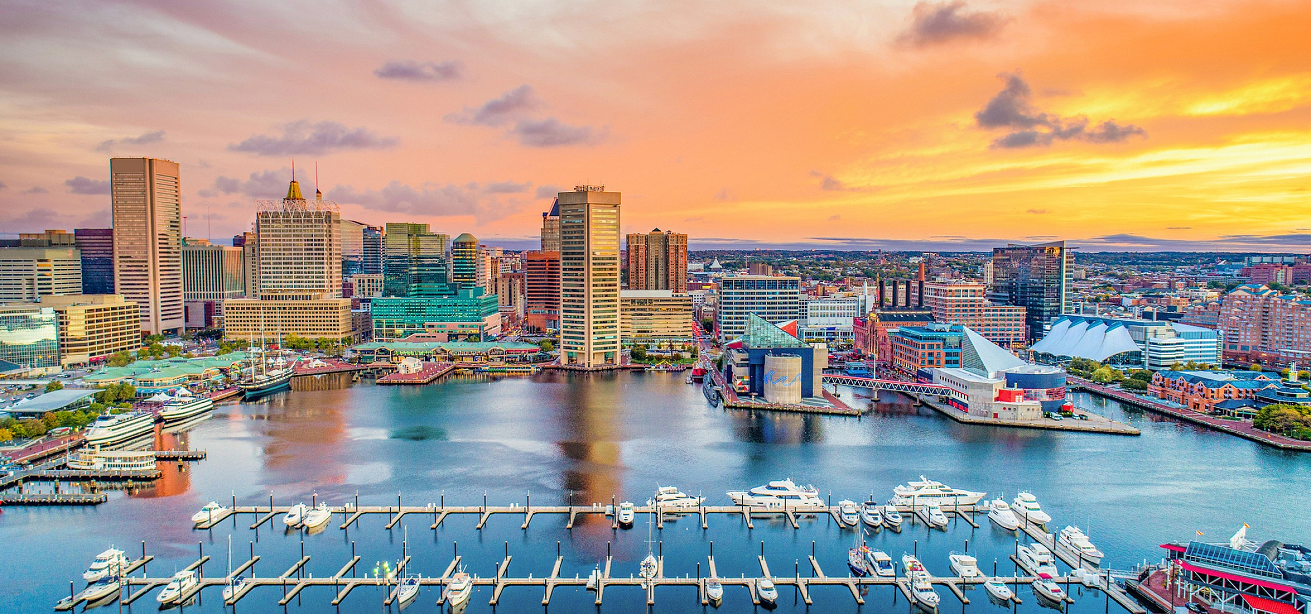 Vibrant cityscape of Baltimore at sunset, featuring a stunning waterfront harbor with yachts and modern architecture.