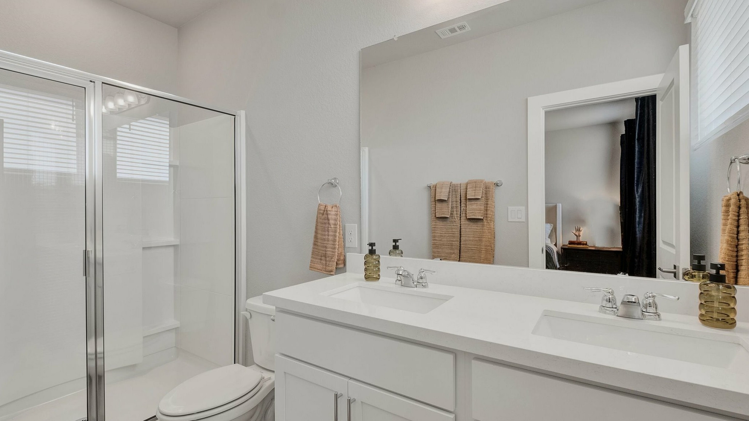 Modern bathroom featuring a spacious glass shower, elegant dual sinks, and stylish light fixtures.