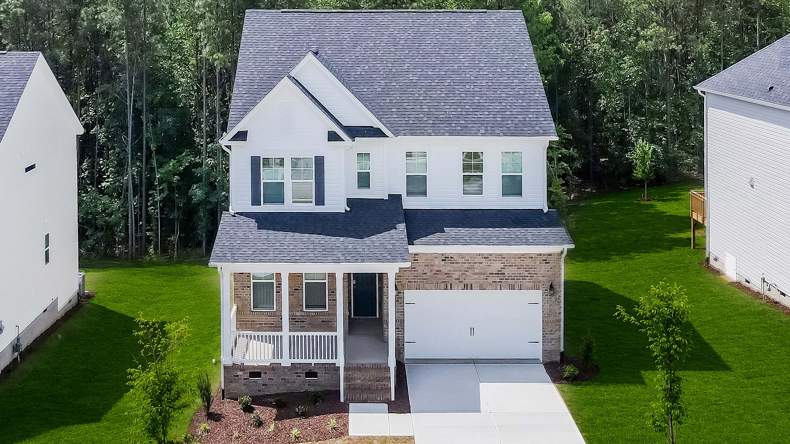 Charming two-story house with a classic brick and white exterior, nestled amidst lush trees, offering a serene and picturesque suburban setting.