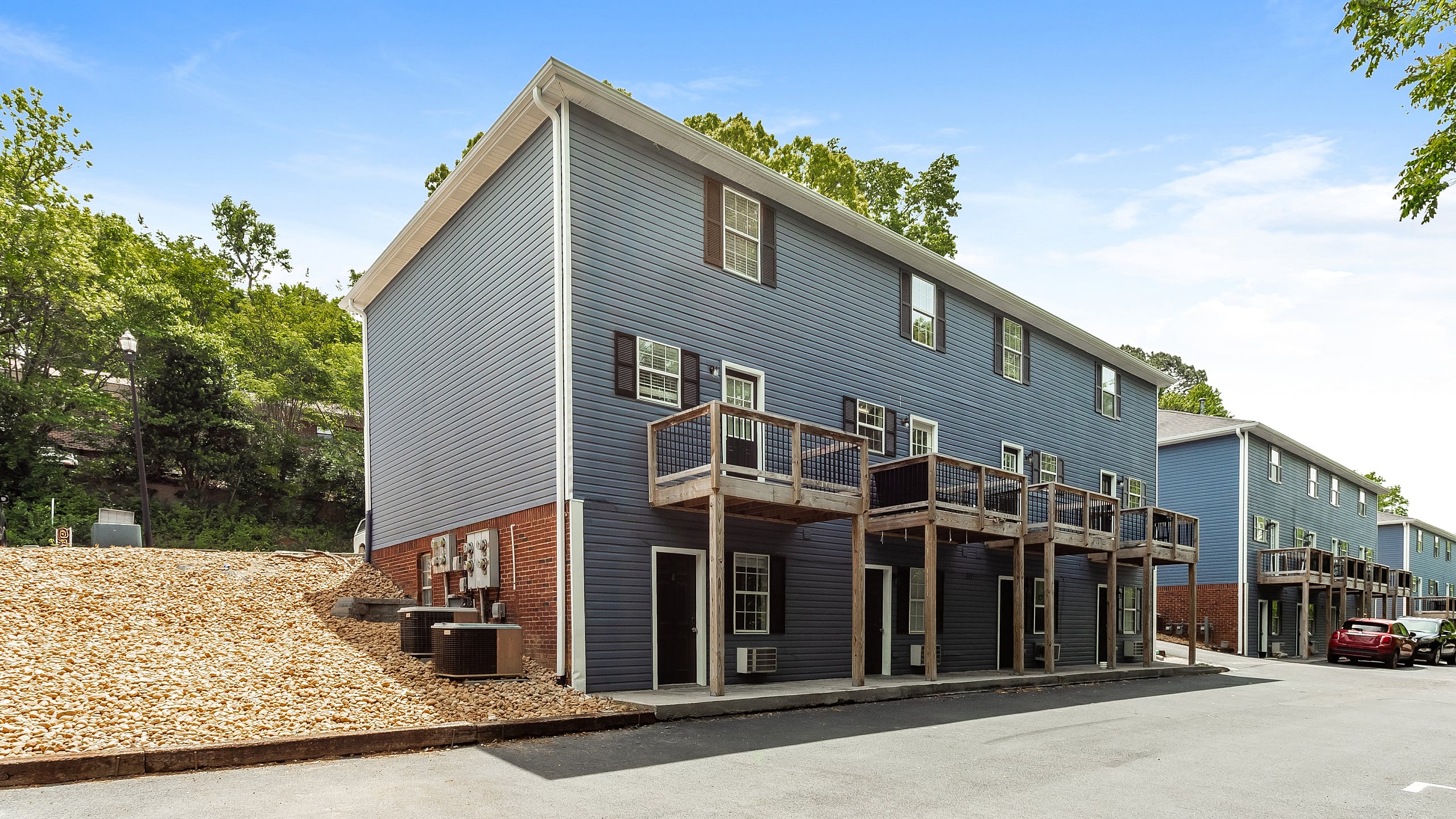 Charming townhouse complex featuring modern blue siding, individual balconies, and scenic wooded backdrop, perfect for comfortable living.