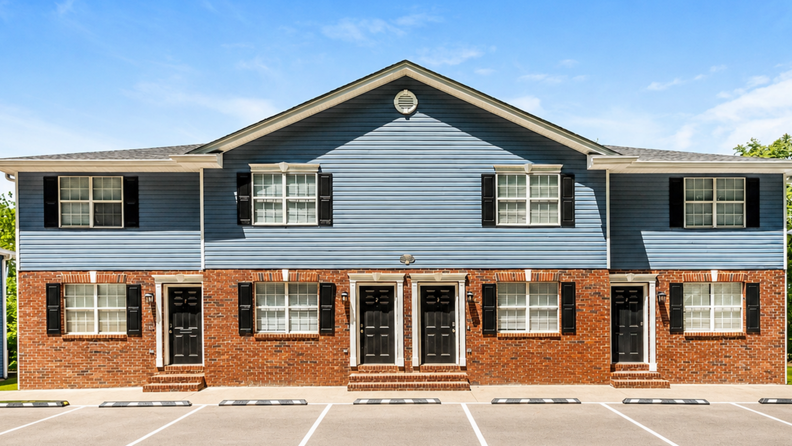 Charming townhouse facade with modern blue siding, brick accents, and ample parking, under a brilliantly clear sky.