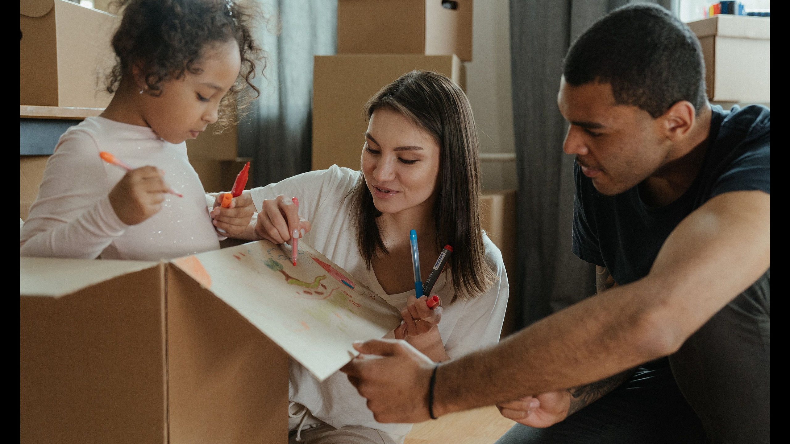 Joyful family engaging in a creative activity together amidst moving boxes, highlighting a fresh start in a new home.