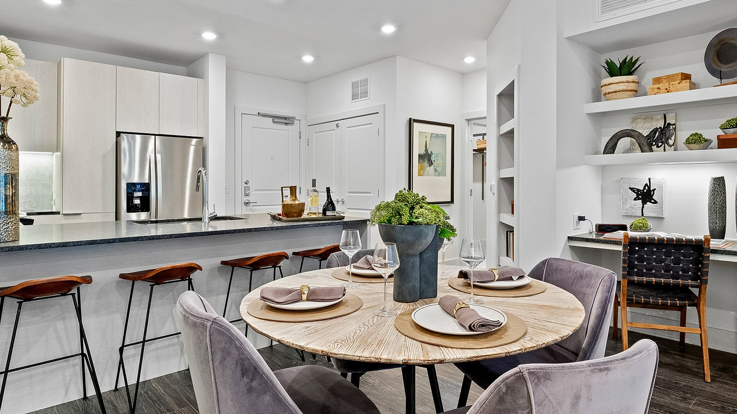Modern open-concept kitchen and dining area with sleek countertops, stylish bar stools, and elegant table setting, emphasizing sophistication and comfort.