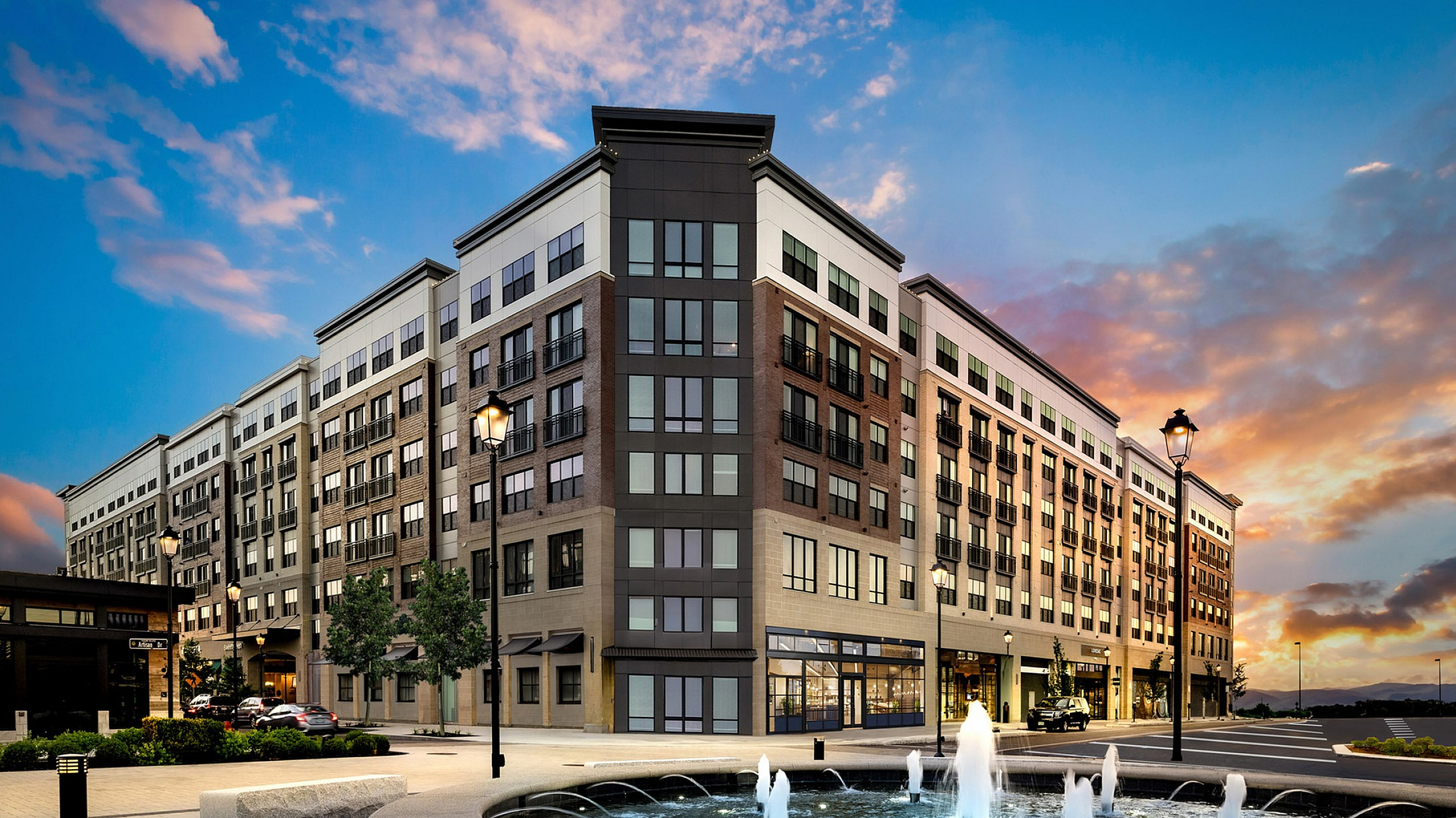 Modern urban apartment complex at sunset, featuring elegant architecture and a scenic water fountain in the foreground.