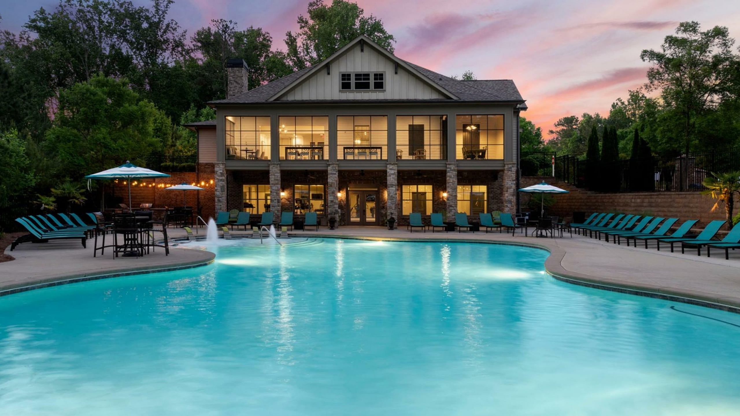 Luxurious apartment complex with a stunning outdoor pool, surrounded by lush greenery and elegant seating areas under a picturesque sunset.