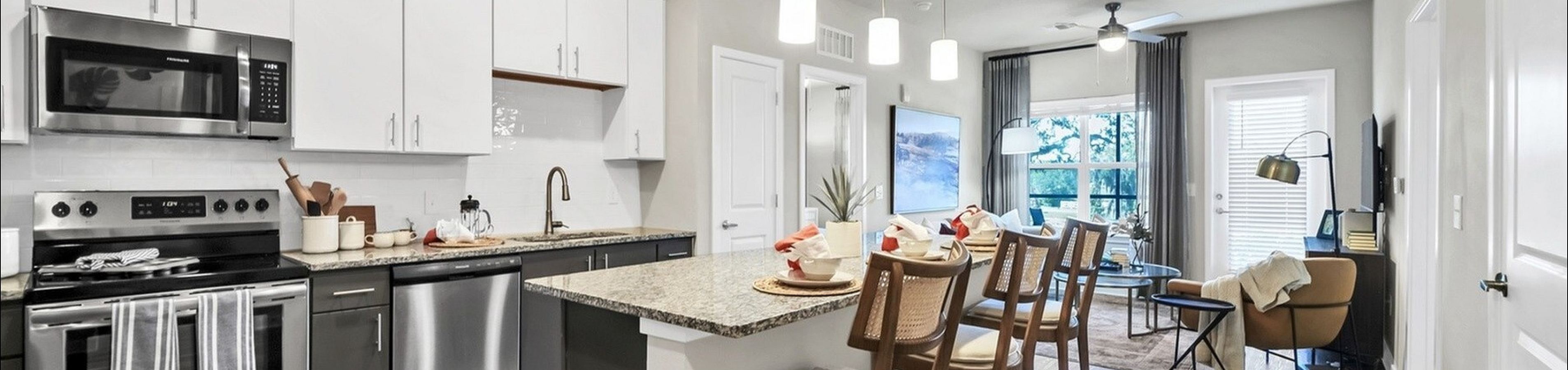 Modern open-concept apartment with sleek kitchen, island seating, and bright living area featuring large windows.