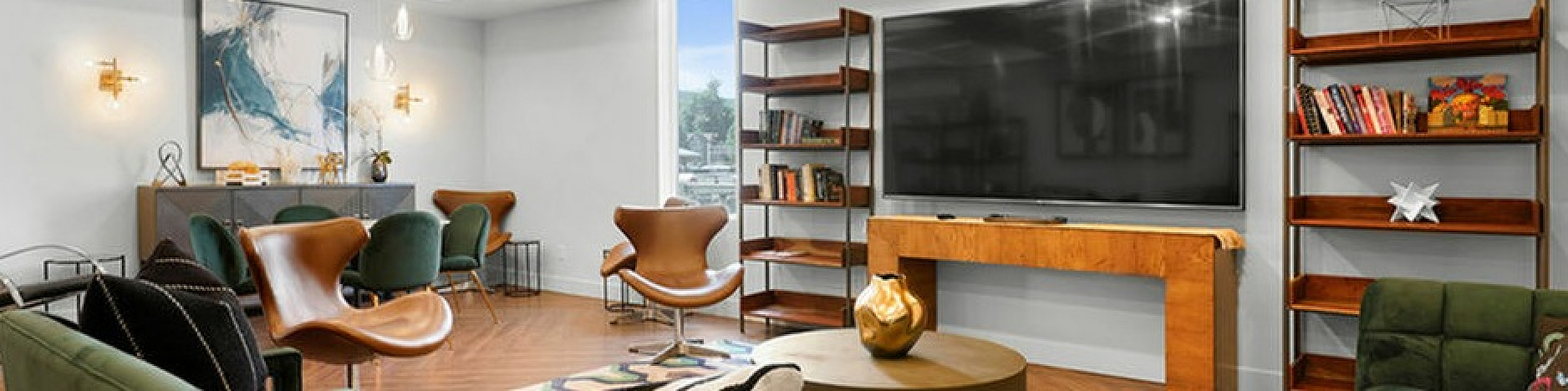 Contemporary living room with elegant green sofas, chic leather chairs, large TV, and stylish bookshelves, creating a warm and inviting atmosphere.
