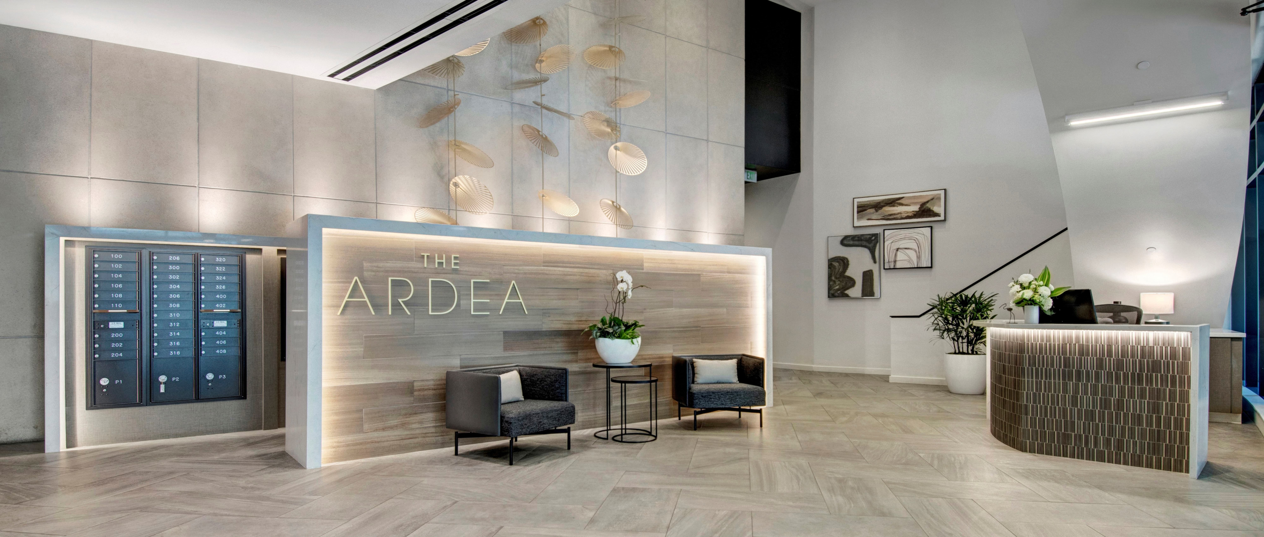 The Ardea Apartment lobby with wood back drop and metal sign with two gray chairs
