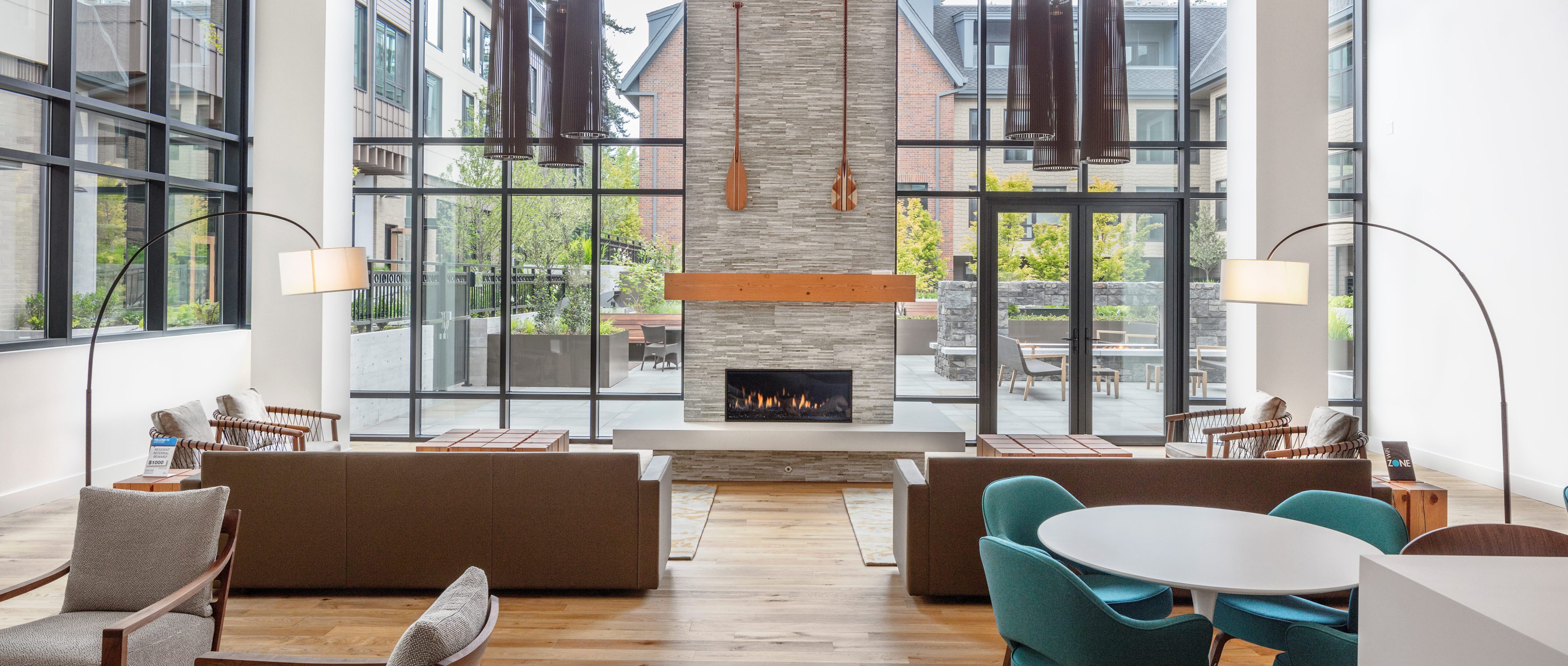 The Windward Apartments lobby with wood floors and green and gray chairs and white table with stone fireplace
