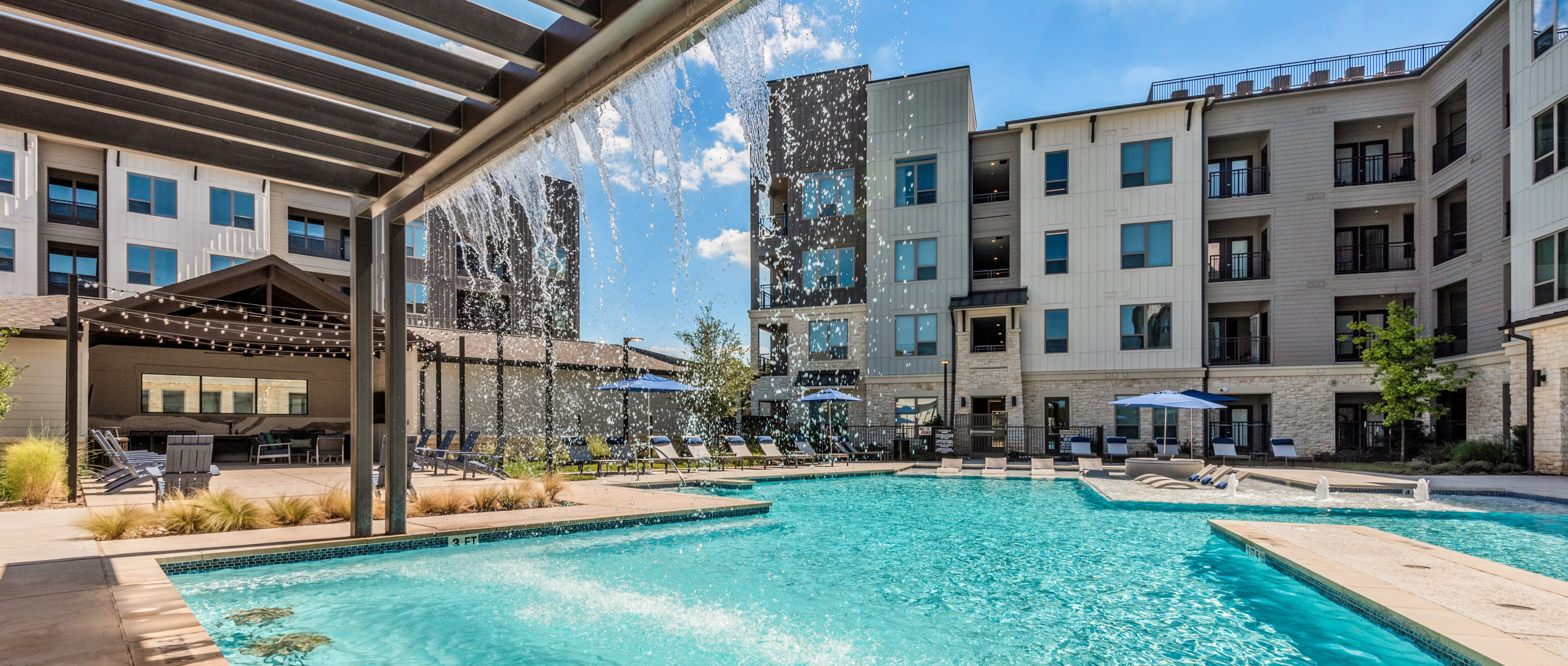 Brightleaf Apartments pool area with overhang and waterfall and chairs around pool area with apartment building in background