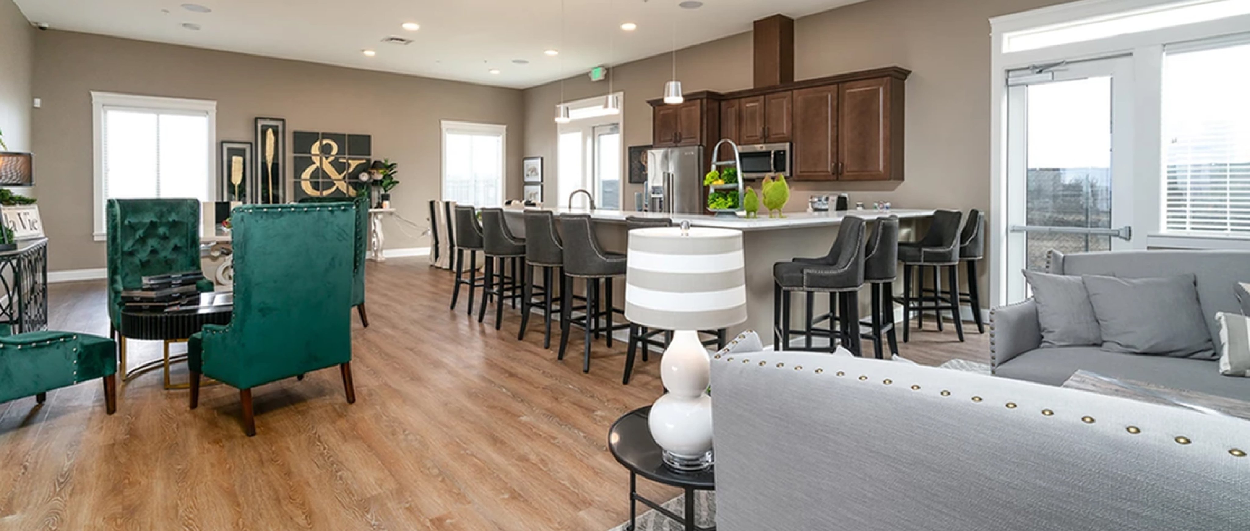 Toscana clubhouse with green fabric chairs around a black table and two gray couches and a bar area with stools and wood cabinets on the otherside