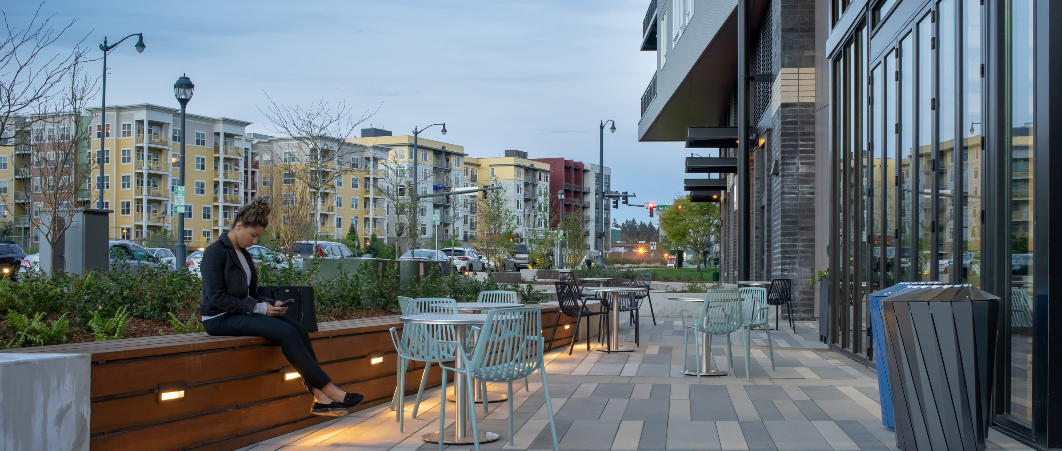 Concrete walking path with metal chairs and women sitting in one and the side of the Heron Flats And Lofts building to side