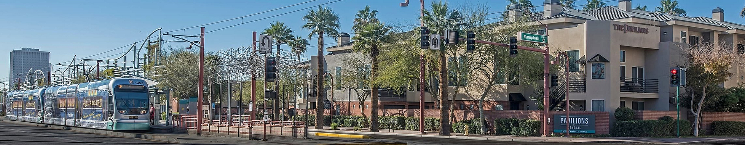 Modern apartment complex with palm trees, situated next to convenient light rail transit in a vibrant urban setting.
