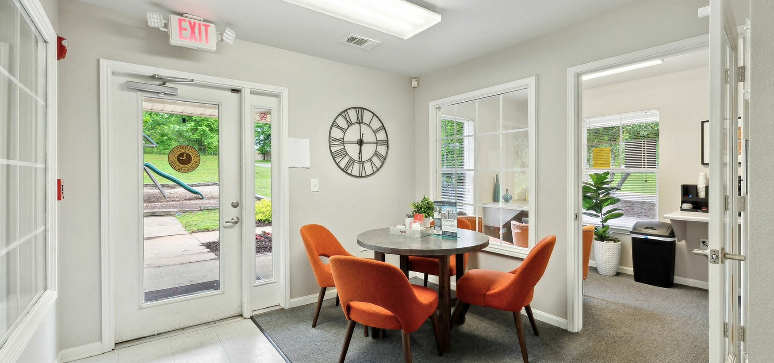 Charming office space featuring vibrant orange chairs around a sleek round table, with large windows offering a view of lush greenery.