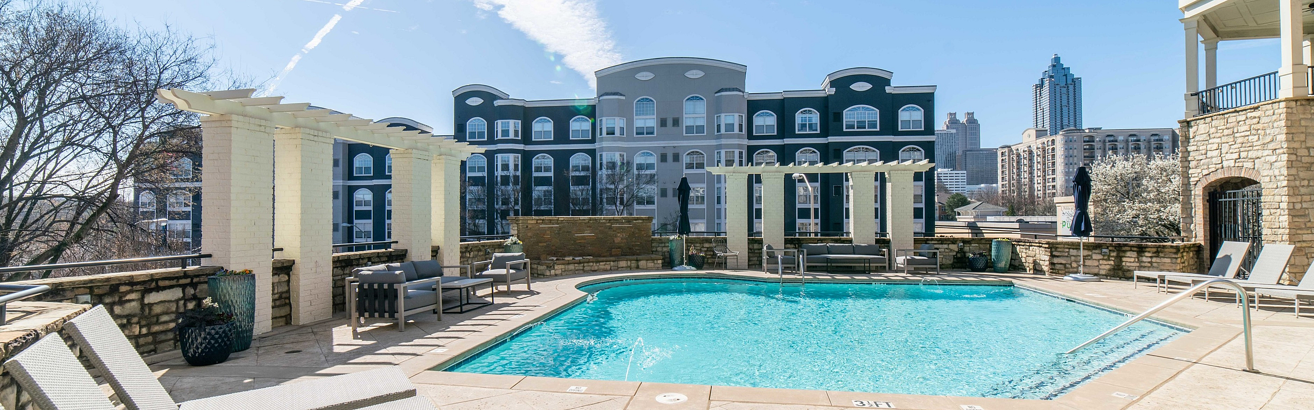 Luxurious apartment complex with a sparkling outdoor pool, stylish seating areas, and stunning skyline views.